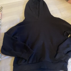 Svart hoodie från H&M - En klassisk svart hoodie från H&M med stor huva och magficka. Tröjan har ribbade muddar vid ärmslut och nederkant, och är tillverkad i mjuk bomullsmix. Perfekt för chill dagar eller när du vill ha en enkel och stilren look.