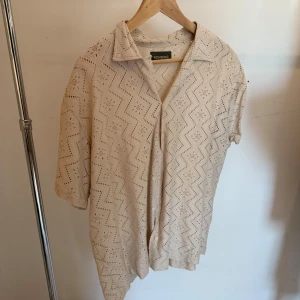 Beige spetsmönstrad skjorta från Ronning - Säljer en beige skjorta från Ronning i storlek L. Skjortan har kort ärm, spetsmönster med zigzag och små blommor, klassisk krage och är tillverkad i bomull och polyamid. Perfekt för dig som gillar en luftig och unik stil.