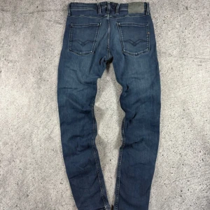 Blå Replay jeans slim fit - Snygga blå jeans från Replay med klassisk femficksdesign och diskreta slitningar. Jeansen har slim passform, raka ben och medelblå tvätt. Märkeslogga på bakfickan och läderpatch i midjan. Perfekta för dig som gillar stilrena och bekväma jeans.