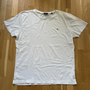 Gant Vit T-Shirt - Gant T-Shirt med broderad logga på bröstet i färgen vit. Storlek: XL, Armhåla till Armhåla: 62.5 cm, Längd: 75 cm, Axel till Armöppning: 20 cm.  Material: 100% bomull.