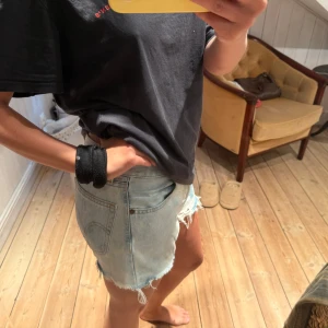 Levi's ljusblå jeansshorts med fransar - Säljer ett par ljusblå jeansshorts från Levi's med slitna kanter och fransar. Klassisk femficksmodell, låg midja och cool tvättad look. Perfekta för sommaren och ger en avslappnad vibe. Levi's patch bak och röd logga på fickan. Oklar storlek men typ S/M