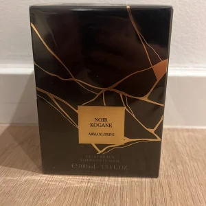 Armani/Privé Noir Kogane EdP 100ml - Exklusiv parfym från Armani/Privé, Noir Kogane, i en lyxig svart och guld kartong. Flaskan rymmer 100 ml Eau de Parfum. Förpackningen har ett elegant, geometriskt mönster i guld mot svart bakgrund och utstrålar premiumkänsla.