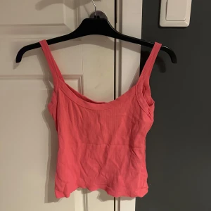 Rosa ribbad linnetopp Vero Moda - Supersöt rosa linnetopp från Vero Moda i ribbad bomull. Modellen är ärmlös med breda axelband och har en lätt croppad passform. Perfekt för varma dagar och enkel att styla med jeans eller kjol.