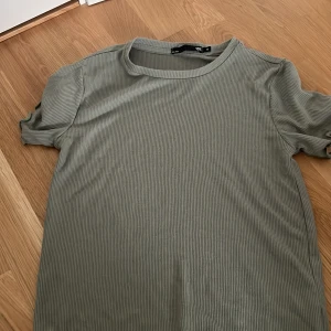 Ribbad grön t-shirt  - Snygg ribbad t-shirt i grönt från lager 157. Modellen är kortärmad med rund halsringning och har en stilren, enkel look. Perfekt för dig som gillar basic men ändå vill ha lite struktur i materialet.