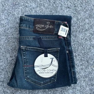  Nya Jacob Cohën Jeans  - Mörkblå jeans från Jacob Cohën i klassisk skinny fit. Snygga detaljer med kontrastsömmar och läderpatch bak. Jeansen är tillverkade i mjukt denimtyg med stretch för extra komfort. Perfekta för dig som gillar en smal siluett och exklusiv känsla.