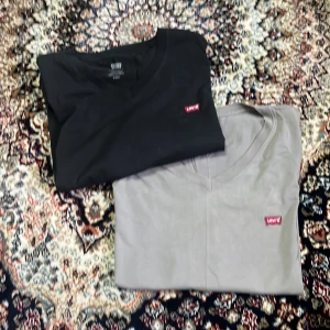 Svart och grå Levi's t-shirt V-ringad - Två stilrena t-shirts från Levi's i svart och grått med klassisk V-ringning och liten röd Levi's-logga på bröstet. Båda är kortärmade och i mjuk bomull, perfekta för en clean och enkel look. Båda två för 100kr.
