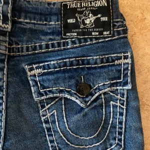 True Religion  jeans blå, stl 32 - Snygga blå jeans från True Religion med riktigt feta bakfickor och med tydliga vita sömmar och knappstängning. Nästan helt nya, användt de typ 5gånger  PRIS KAN DISKUTERAS