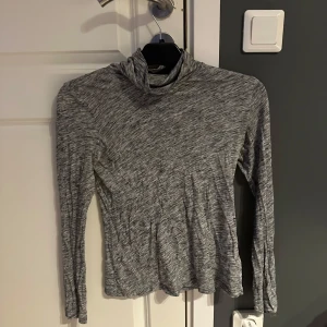Gråmelerad polotröja från Lindex - Säljer en tunn och mjuk gråmelerad polotröja från Lindex i storlek S. Tröjan har lång ärm och en hög krage som ger en clean och stilren look. Perfekt att styla med jeans eller kjol för en chill vibe.