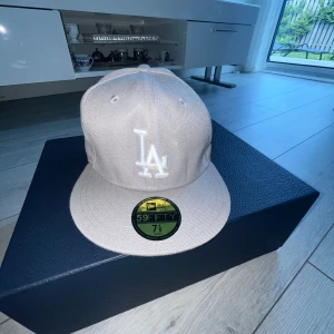 Beige LA keps från New Era 59FIFTY - Säljer en beige LA keps från New Era 59FIFTY med broderad LA-logga framtill och World Series-märke på sidan. Kepsen har platt skärm och klassisk passform. Perfekt för dig som gillar stilrena accessoarer.