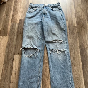 Ljusblå ripped jeans från Gina Tricot  - Ljusblå jeans med raka ben och stora slitningar på båda benen. Klassisk femficksmodell med hög midja och coolt avslappnat uttryck. Perfekta för en streetstyle-look och tillverkade i robust denim. Är lite loosefit men sitter bra runt rumpan.