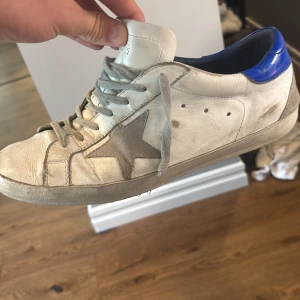 Golden Goose vita sneakers med blå detalj - Golden Goose skor relativt nya den ena skorn är i perfekt sick medans den andra har tappat sulen detta är möjligt att fixa hos en sko makare för ca 500 kr 