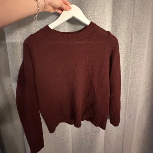 Mörkröd stickad tröja med rund hals - En enkel och snygg mörkröd stickad tröja med rund halsringning och långa ärmar. Tröjan har ribbade muddar vid ärmslut och nederkant, perfekt för lager-på-lager under kyliga dagar.