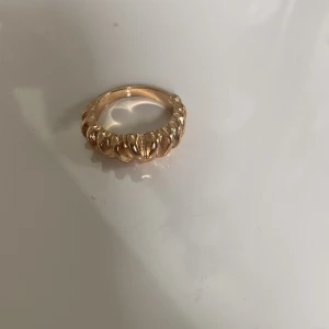 Guld ring - Säljer en chunky ring i guldpläterad metall med ett coolt, räfflat mönster runt hela ringen. Perfekt statement-piece för dig som gillar att sticka ut med dina accessoarer. Ringen har en rund, fyllig form och glänser snyggt i ljuset.