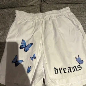 Shorts  - Superfina vita shorts med söta fjärilstryck och texten “dreams” – perfekta för sommarens alla outfits! Bekväma och lätta att styla med både enkla toppar eller färgglada plagg. Shorts i bra skick, redo för en ny garderob.