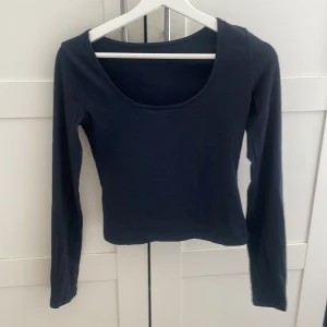 Mörkblå långärmad rygglös topp - En enkel och stilren mörkblå långärmad topp med urringning i ryggen. Perfekt att matcha med både jeans och kjol för en trendig look.