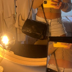 Svart axelväska med kedjerem - Säljer en svart axelväska i skinn med bred lockstängning och silverfärgad kedjerem. Väskan har en stilren och enkel design🙌🏼🙌🏼