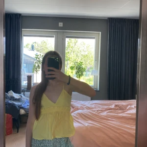 Gul linnetopp från Zara - Säljer en söt gul linnetopp från Zara med smala axelband och v-ringning. Toppen har en luftig passform med rynkad midja och lätt volang nedtill. Perfekt för varma dagar och enkel att matcha med shorts eller kjol.