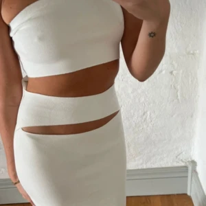 Vit klänning med cut out-detaljer - Säljer en vit långklänning med tight passform och trendiga cut out-detaljer i midjan. Klänningen är gjord i ett stretchigt material som sitter snyggt på kroppen. Perfekt för sommaren eller festliga tillfällen.