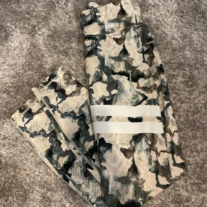 Camo-mönstrade tights från Stronger - Träningstights från stronger, hög i midjan och har en liten ficka längst upp bak till tex nycklar, hörlurar eller liknande. Andväd fåtal gånger.