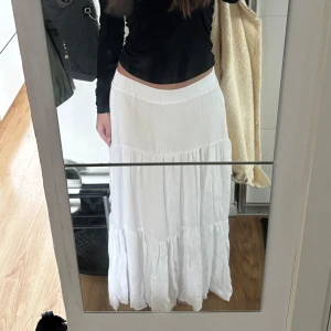 Vit långkjol med volang - Säljer en vit långkjol med bred resår i midjan och volangdetaljer. Aldrig använd innan och lappen sitter kvar!! Den går ända ner till marken vid långmidjat (163cm). Jättefin sommarkjol till varmare dagar. 