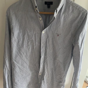 Blårandig skjorta från GANT - Snygg blårandig skjorta från GANT med klassisk krage och broderad logga på bröstet. Skjortan har långa ärmar och knäppning framtill. Perfekt för en stilren och tidlös look.