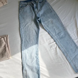 Ljusblå jeans med slits vid benslut - Säljer ett par ljusblå jeans med klassisk femficksdesign och slits vid bensluten. Jeansen har normal passform och är raka i modellen. Perfekta för dig som gillar en enkel men trendig look.