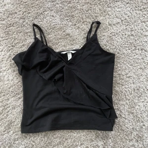 Svart linnetopp med volang från H&M - Säljer en svart linnetopp från H&M med smala axelband och snygg volangdetalj framtill❤️
