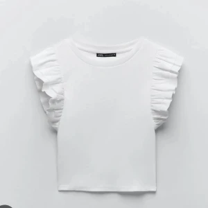 Vit topp med volangärmar från Zara - Säljer en vit topp från Zara med korta volangärmar. Toppen är ribbad och har en rund halsringning. Perfekt för en trendig och stilren look.