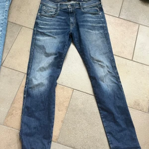 Replay Anbass jeans i blå denim - Säljer ett par Replay Anbass jeans i klassisk blå denim med lätt slitning framtill. Byxorna har fem fickor, dragkedja och knapp i midjan. Perfekta för dig som gillar en tidlös jeanslook.