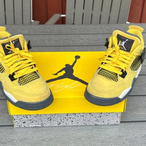Nike Air Jordan 4 Retro 'Lightning' GS - Gula Nike Air Jordan 4 Retro 'Lightning' GS sneakers med svarta och vita detaljer. Skorna har snörning, meshpaneler på sidorna och en platt sula. Ikonisk Jumpman-logga syns på plösen och sulan. Perfekta för dig som vill sticka ut med färg. Skick enligt bilder, hör gärna av dig vid funderingar 😁! 