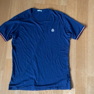 Mörkblå T-shirt från Moncler  - Säljer nu en stilren mörkblå T-shirt från Moncler som passar perfekt inför våren. Tröjan passar Både M/L. Hör gärna av dig om du har fler frågor! 