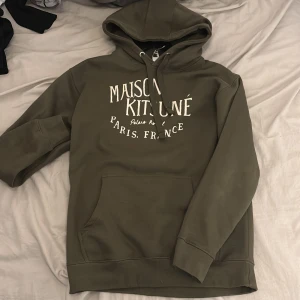  hoodie från Maison Kitsuné - Säljer en olivgrön hoodie från Maison Kitsuné med vit text på bröstet. 