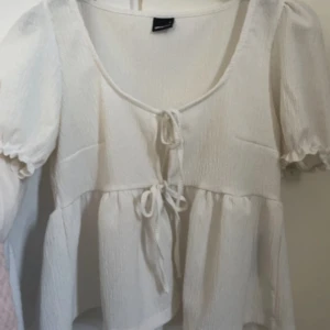 Vit blus med knyt från Gina Tricot - Supersöt vit blus från Gina Tricot med två knyt framtill och puffiga korta ärmar. Blusen är aldrig använd endast testad, den har aldrig blivit använd då den var för stor på mig. (Pris kan diskuteras)