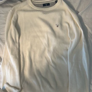 Vit stickad tröja från Gant - Säljer en stilren vit stickad tröja från Gant med broderad logga på bröstet. Tröjan har rund halsringning och långa ärmar. Perfekt för en klassisk och enkel look.