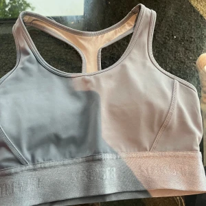 Grå sport-bh från STRONGER - Säljer en sport-bh från STRONGER i ljusgrått/ljusblå. Modellen har brottarrygg och bred resår nedtill med logga. Endast använd en gång. Skriv till mig för frågor😊🫶🩷