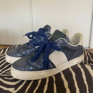 Blå glittriga sneakers från Valentino Garavani Flycrew - Säljer ett par blå sneakers från Valentino Garavani Flycrew med glittrig ovandel, vita detaljer och blå snörning. Köpte skorna 2017 men inte varit använda på länge. Har därmed inte kvar lådan. En nit saknas. Skriv till mig för fler bilder!🥰