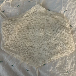 Vit virkad croppad linnetopp - Säljer en virkad vit  linnetopp med knytband i ryggen. Toppen har en spetsig nederkant och är ärmlös, perfekt för varma dagar. Materialet är mjukt och luftigt. 