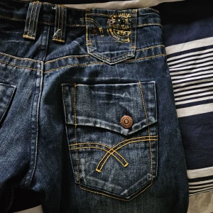 Mörkblå jeans - Säljer ett par mörkblå jeansbyxor från Solid Jeans med snygga kontrastsömmar och stora bakfickor med knapp och dekorativ gul söm. Byxorna har klassisk femficksdesign och raka ben. Tillverkade i 100% bomull. W31/L34 priset går att diskutera