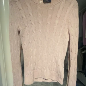 Ljusrosa kabelstickad tröja från polo Ralph Lauren - Säljer en ljusrosa kabelstickad tröja från polo Ralph Lauren. Tröjan har rund halsringning, långa ärmar och klassiskt kabelstickat mönster. Perfekt för dig som gillar en tidlös och stilren look. Den har dock fläckar (se bild) därför säljs den billigt.