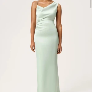 Adoore Almeria - Light Sage - Säljer en elegant ljusgrön långklänning med oneshoulder och smal passform. Klänningen har en draperad överdel och smala axelband, vilket ger en stilren och modern look. Perfekt för bal/bröllop/sommarfesten. Har använts enbart en gång.