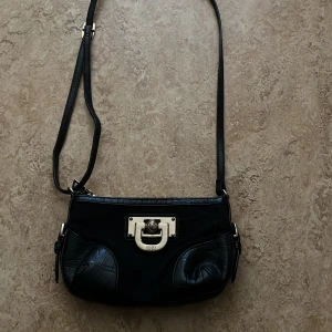 Svart axelväska  - DKNY väska, får plats med det mesta även om den ser liten ut. Har haft den i några år men den är varken jätte trasig. Har inte använt så många gånger kanske 20 gånger men har haft den ett tag. Har bara använt när jag ska ska ut med familj eller vänner. 