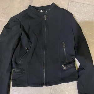 Svart jacka med dragkedjor - Säljer en svart jacka med flera dragkedjor framtill och på fickorna. Jackan har en rak passform och lång ärm, perfekt för dig som gillar en stilren och edgy look. Stängs med dragkedja hela vägen upp till halsen. Storlek XL men är lite för stor för en tjej som bär på xs. 