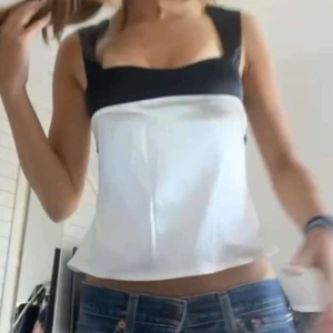 SvartVit topp - Säljer en snygg svartvit linnetopp med breda svarta axelband och svart kant upptill. Passar XS/S. Aldrig använt. Kan gå ner i pris. Toppen har en rak passform och är tillverkad i ett glansigt material som ger en stilren look. 