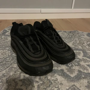 Svarta Nike Air Max 97 sneakers - Säljer ett par helsvarta Nike Air Max 97 sneakers som har använts helt okej mycket, den ända defekten är att ena sulan har poppats men det syns knappast, säljer eftersom de inte passar mig längre. Skriv till mig om ni har frågor! Vid snabb affär kan vi diskutera priset. Vill gärna att ni väljer instabox!