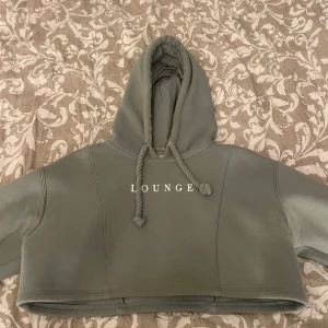 Ljusgrön croppad hoodie från Lounge - Säljer en croppad hoodie från Lounge med huva och grova dragsnören. Tröjan har långa ärmar och ribbade muddar. Perfekt för en avslappnad stil och riktigt skön att ha på sig.