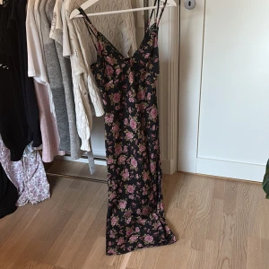 Svart blommig långklänning med spetsdetaljer - Köpte för ca 600-650kr. Säljer en svart långklänning med rosa blommor. Klänningen har smala axelband, v-ringning och spetsdetaljer vid bysten. Materialet är mjukt och följsamt, perfekt för sommarens varma dagar. Säljer då denna eftersom den är för liten, klänningen har bara används fåtal gånger❣️