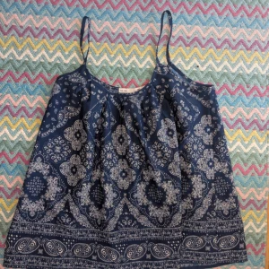 Mörkblå mönstrad linnetopp - Säljer en mörkblå linnetopp med tunna axelband och vitt paisleymönster. Toppen har en luftig passform och är perfekt för varma dagar. Superfin till både jeans och kjol!