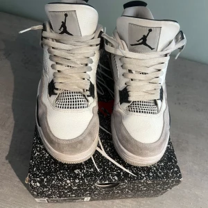 Nike Air Jordan 4 Retro White/Black - Säljer ett par Nike Air Jordan 4 Retro i vitt, svart och grått. Skorna har klassisk meshpanel, snörning och Jumpman-logga på plös och häl. Stilren design med kontrasterande detaljer och bekväm passform.