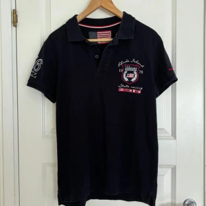 Newport piké - Detta är min brors mörkblå piké från märket Newport. Han har vuxit ur den och använder den därför inte längre. Den har ett flertal tryck; dels på respektive arm, dels på bröstet och ryggen. Den är i gott skick utan några defekter.