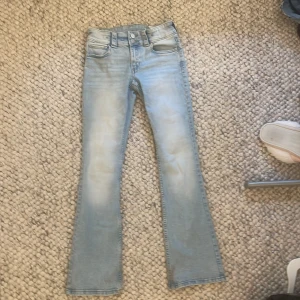 Ljusblå bootcut jeans från H&M - Säljer ett par ljusblå bootcut jeans från H&M med låg midja och justerbar midja. Jeansen har klassiska fickor fram och bak med lock och knapp på bakfickorna. Perfekta för dig som gillar en retro vibe. 